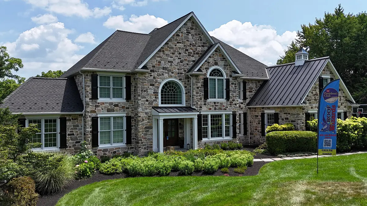 Stone-front home with a dark shingle roof and metal roof accents